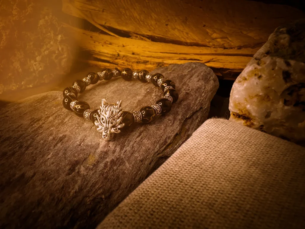 Beaded bracelet with a detailed silver wolf head centerpiece, resting on textured stone surrounded by rugged wood, quartz, and canvas