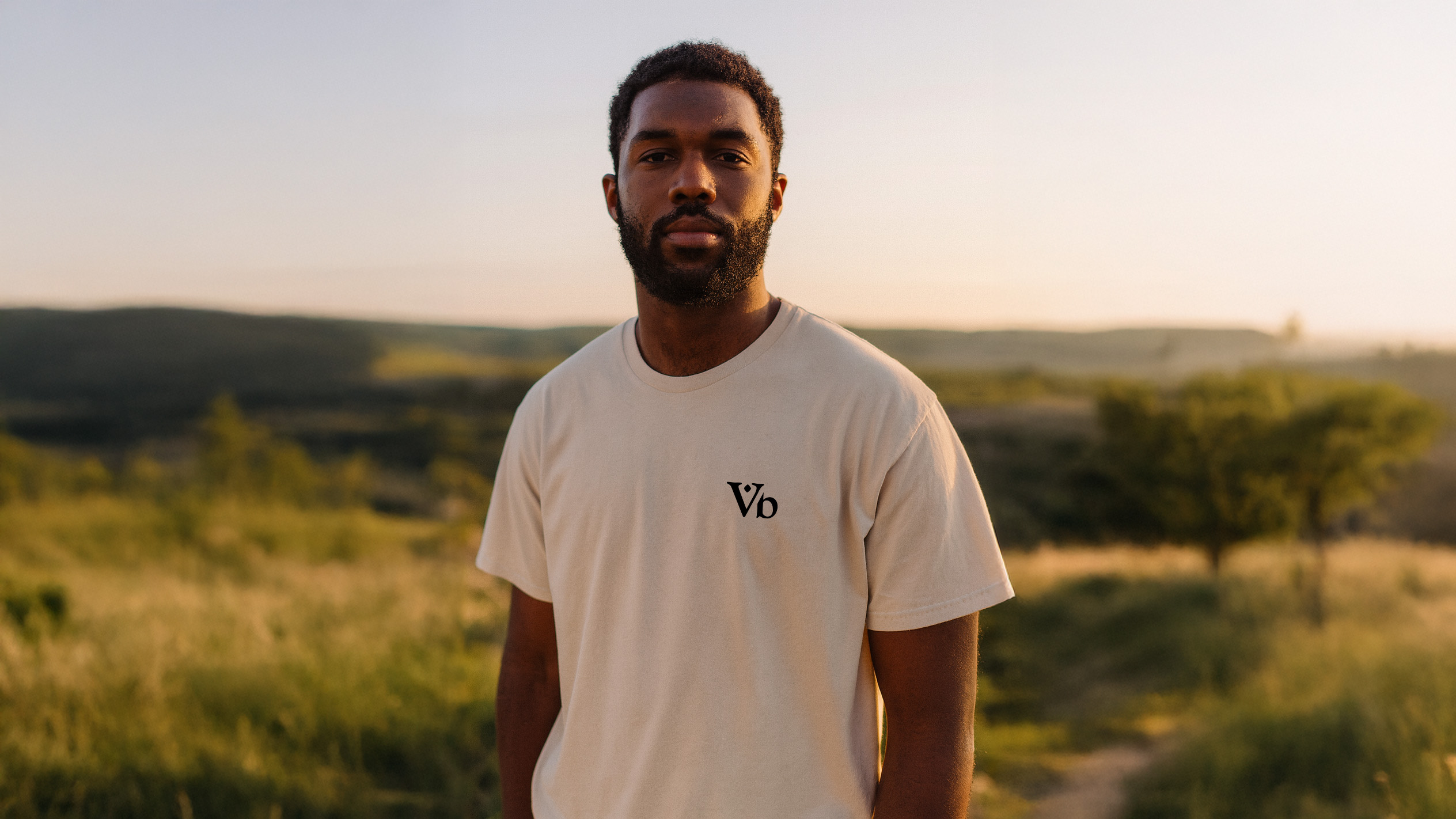 Man outdoors at golden hour wearing the Varbridge VB-0524 Field Unit natural tee with minimalist Vb chest logo - durable, understated t-shirt for everyday wear with a tactical edge.
