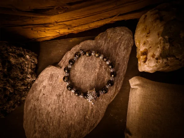 Overhead view of a beaded bracelet featuring a silver wolf head, laid on a flat stone surface and surrounded by rugged textures