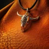 Silver longhorn skull pendant on a black cord, displayed against rich textured brown leather with warm, directional lighting.