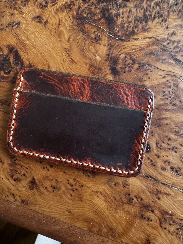 Handcrafted leather cardholder with burnished edges and visible patina, resting on a richly textured wooden surface.