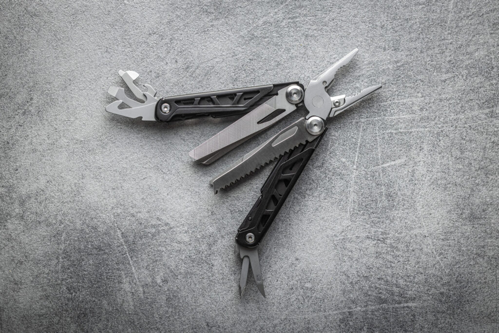 Stainless steel multitool with pliers, knife, and other tools on a grey textured background – ideal gift for outdoorsy men