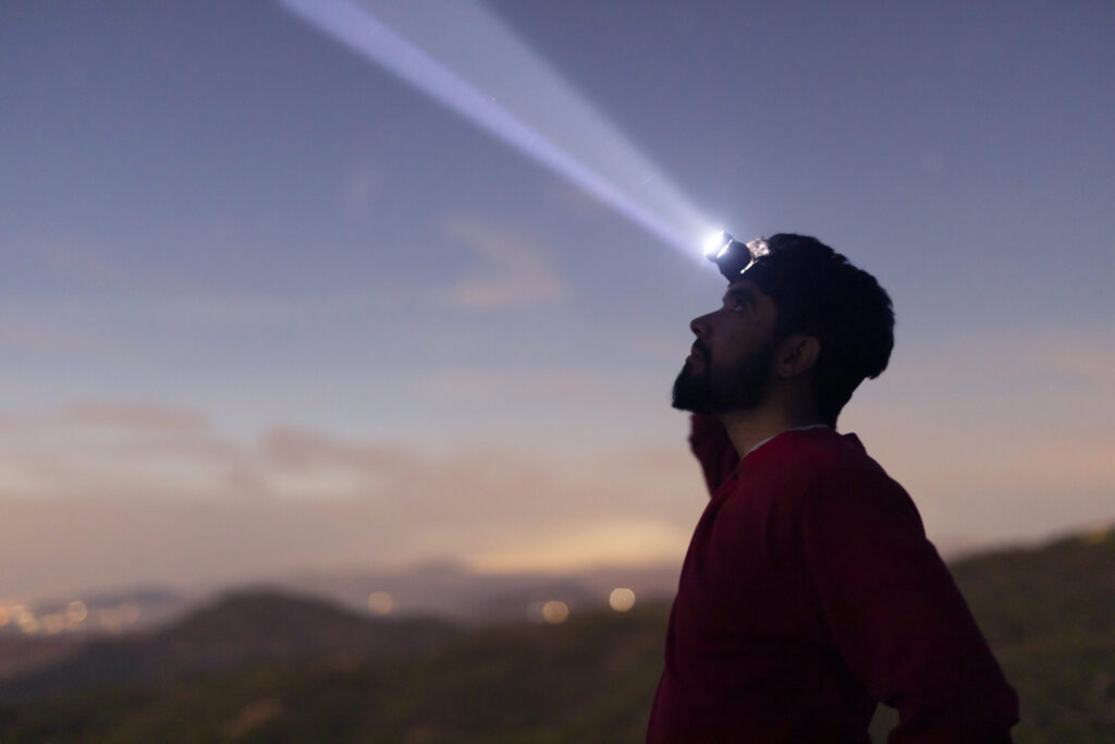 Man wearing a headlamp outdoors at dusk, shining a bright beam of light—essential hands-free gear for camping, hiking, and outdoor adventures