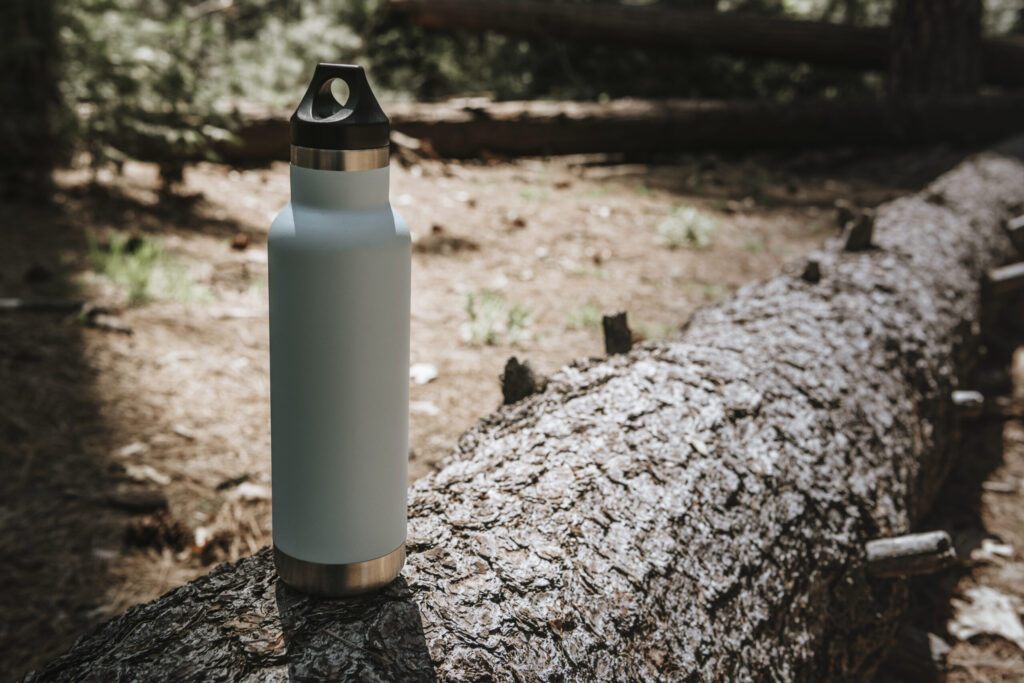 Stainless steel insulated water bottle on a tree trunk in the forest – essential outdoor gear and practical gift for adventurers
