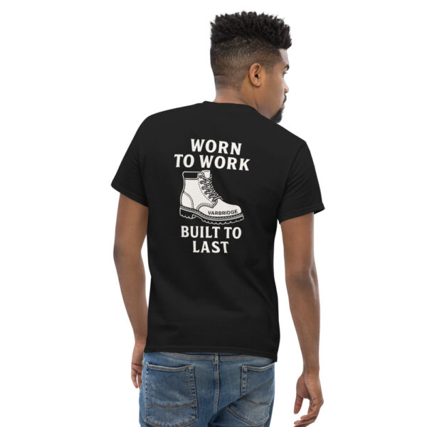 Man wearing black Varbridge t-shirt with illustrated work boot and bold white text reading “WORN TO WORK – BUILT TO LAST” on the back, looking over shoulder while walking