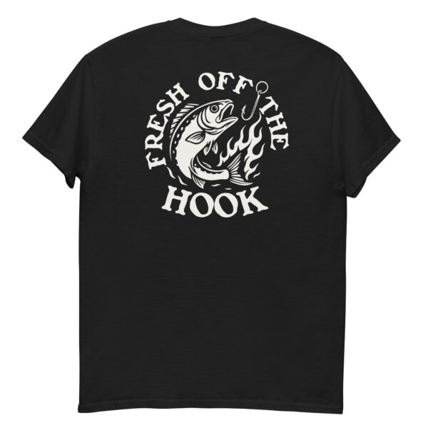 Back view of a black t-shirt laid flat, featuring a bold white graphic of a fish leaping from flames toward a fishing hook, with the phrase “FRESH OFF THE HOOK” surrounding the design.