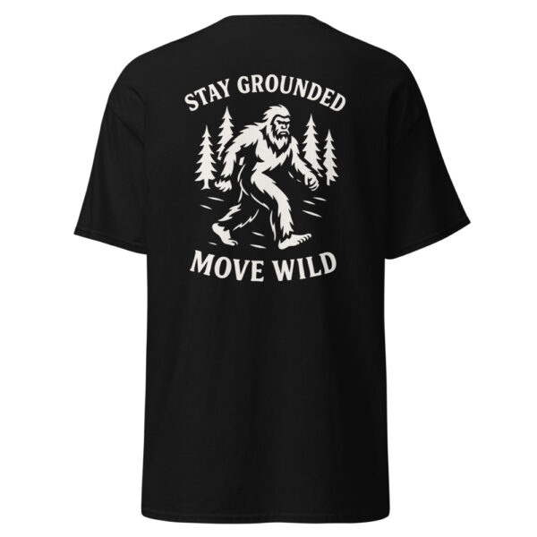 Back view of a black t-shirt featuring a white graphic of Bigfoot walking through a forest with pine trees, surrounded by the phrase “STAY GROUNDED MOVE WILD.”