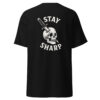 Back view of a black t-shirt with a white graphic design featuring a skull impaled by a tactical knife and the phrase “STAY SHARP” in bold curved text above and below the illustration.