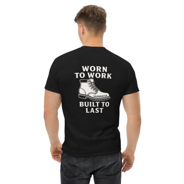Man wearing black Varbridge t-shirt featuring rugged work boot graphic and bold text reading “WORN TO WORK – BUILT TO LAST” on the back, standing with hands relaxed