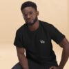 Man wearing black Varbridge t-shirt with minimalist Vb logo on the chest, seated in front of neutral beige background, casual and confident pose