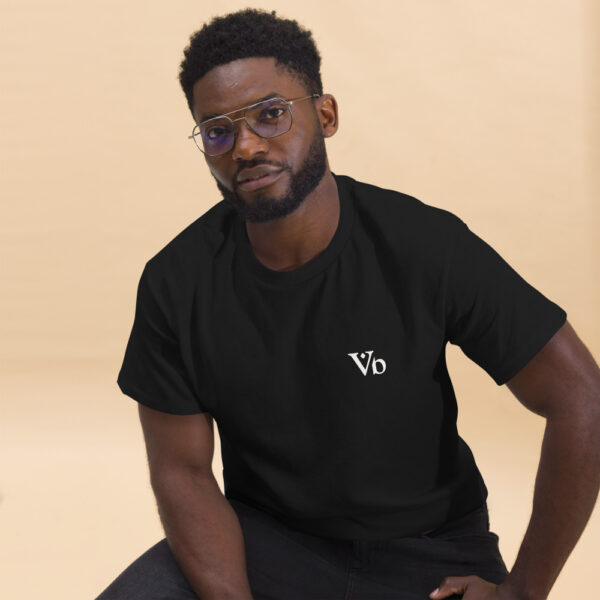 Man wearing black Varbridge t-shirt with minimalist Vb logo on the chest, seated in front of neutral beige background, casual and confident pose